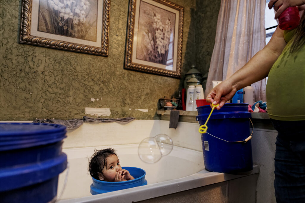 child in blue bucket of water in bathtub with bubbles floating in the air