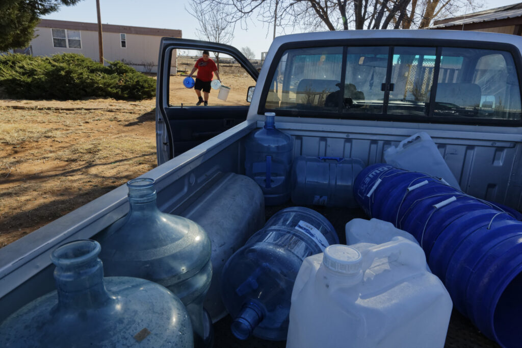 pick up truck filled with empty plastic bottles and a person carrying jugs framed in truck window