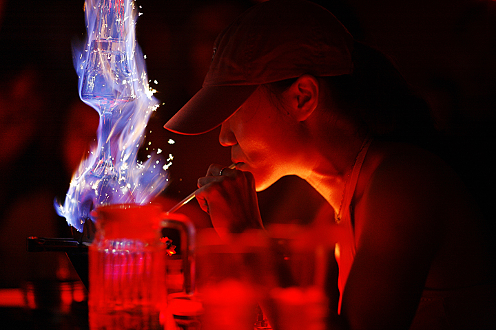 Blue flames shoot up from a bright red drink that lights up a person at a bar