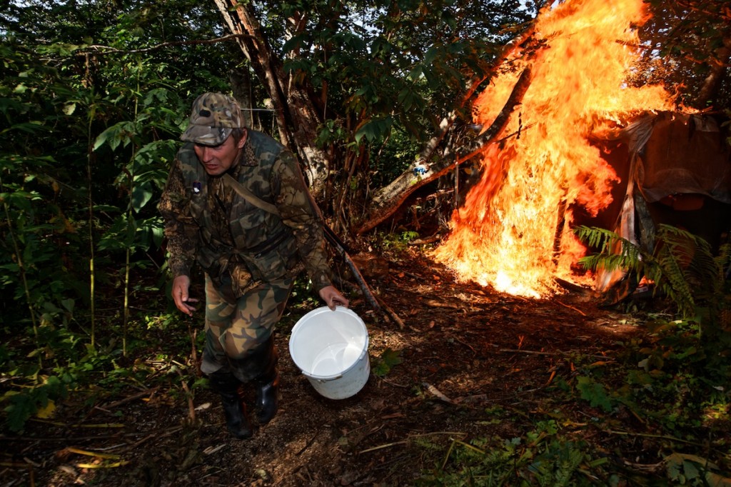 Man in camouflage walks away from flames in a wooded area