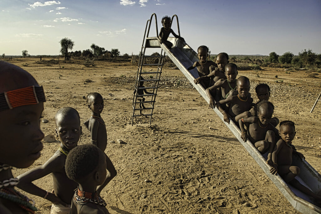 many African children on a playground slide in a desolate landscape